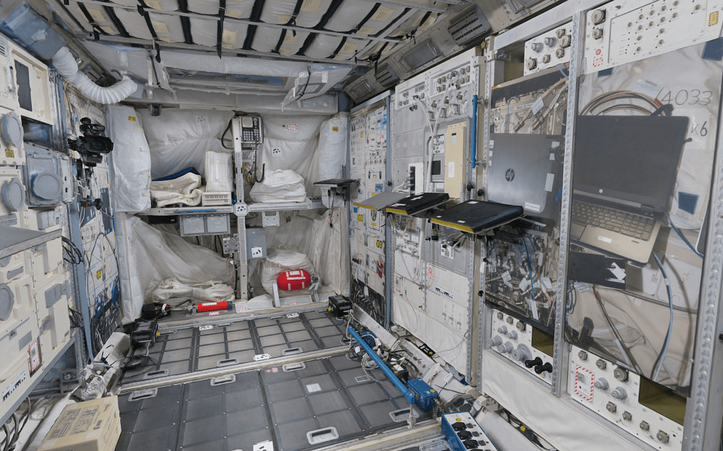 Interior view of a space module showcasing various scientific equipment, computers, and tools against a backdrop of white coverings and walls filled with technical panels.